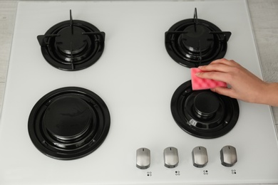 Photo of Woman cleaning gas stove with sponge, closeup