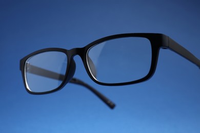 Photo of Stylish pair of glasses with black frame on blue background, closeup