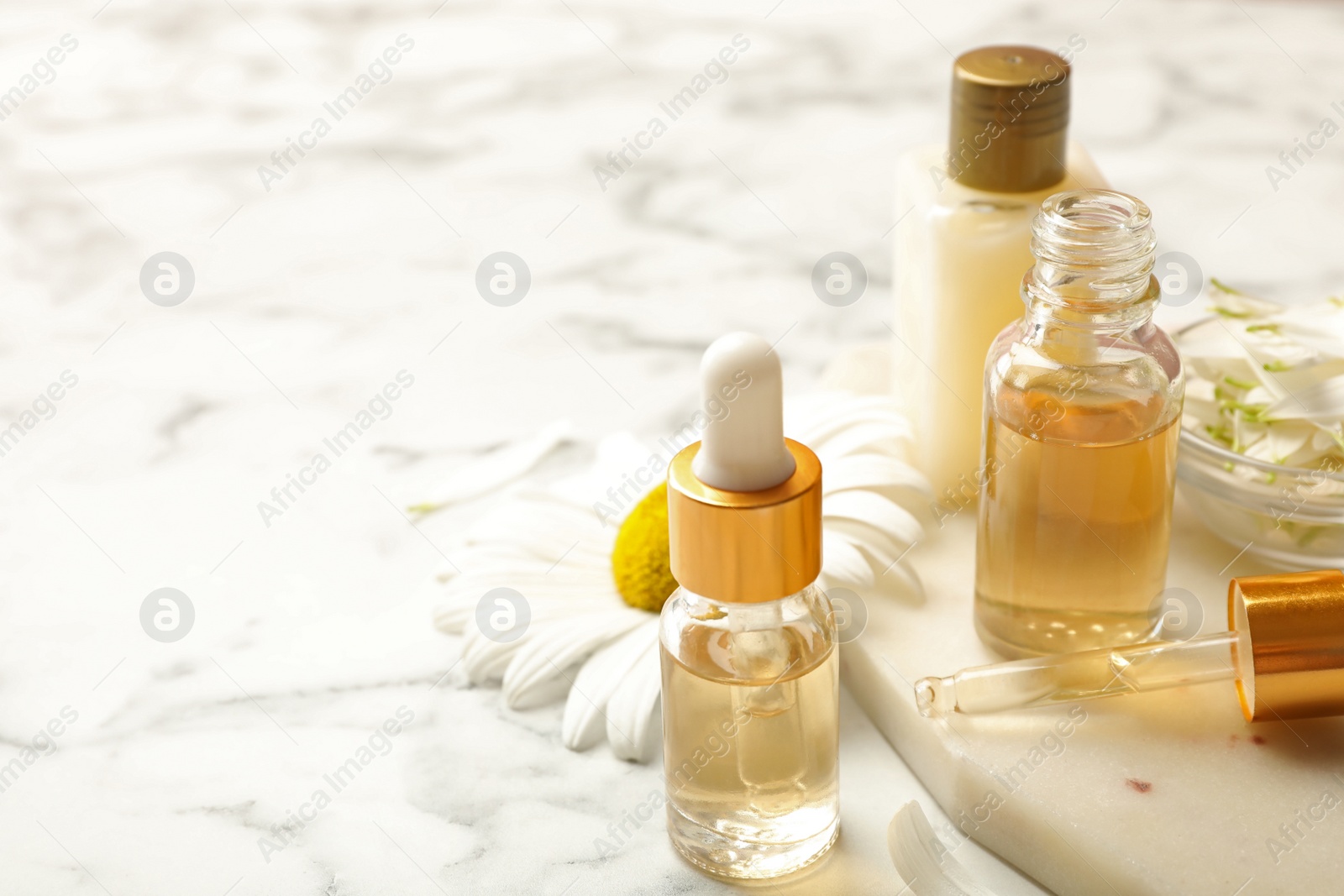 Photo of Chamomile and cosmetic products on white marble table. Space for text