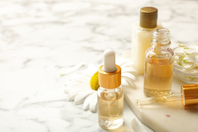 Chamomile and cosmetic products on white marble table. Space for text