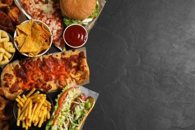 Burger, pizza and other fast food on black table, flat lay with space for text