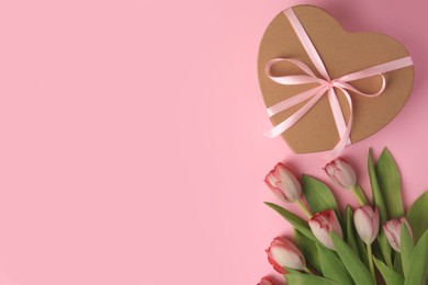 Photo of Heart shaped gift box with bow and beautiful tulips on pale pink background, flat lay. Space for text