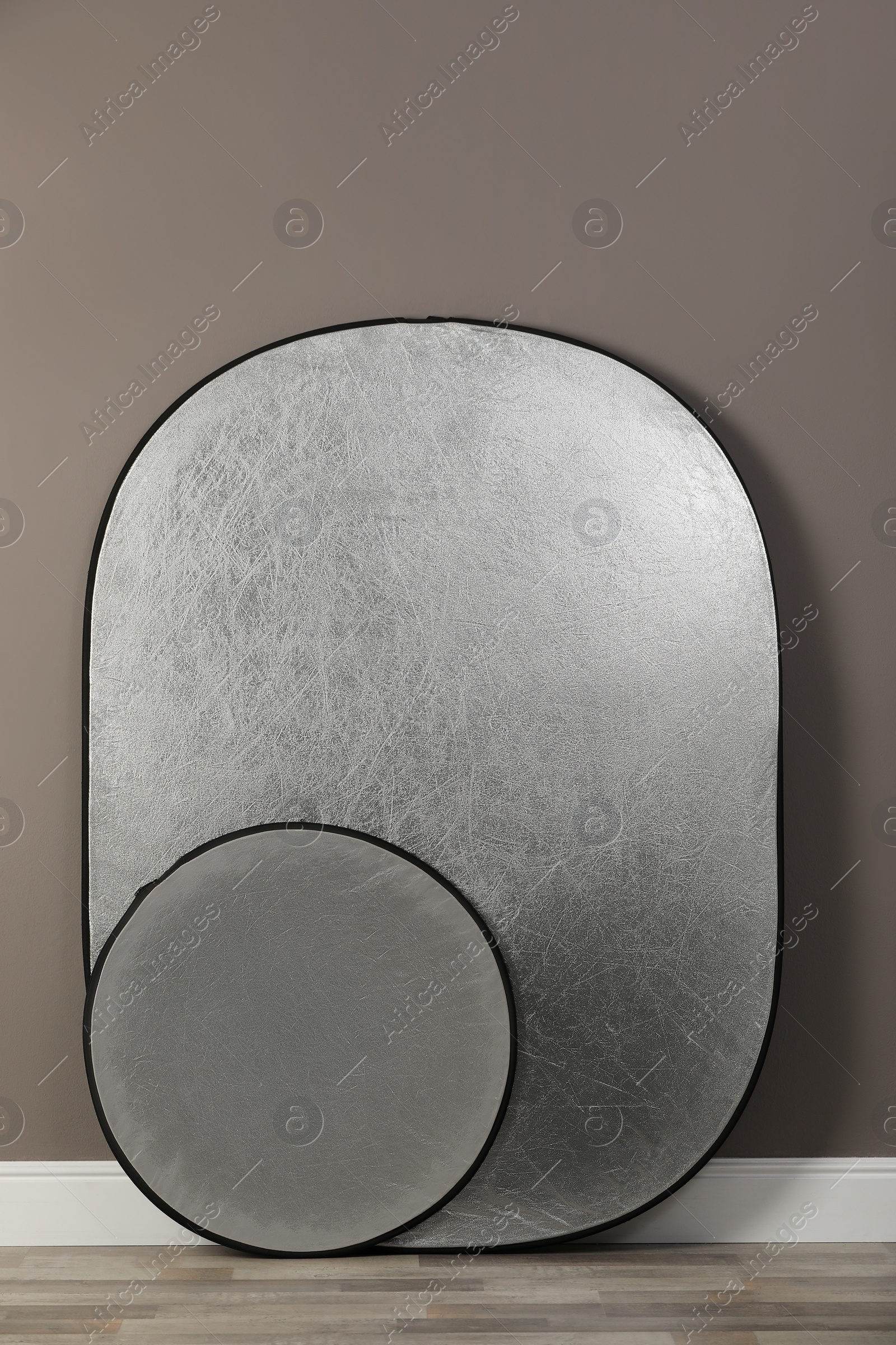 Photo of Professional silver reflectors near grey wall in room. Photography equipment