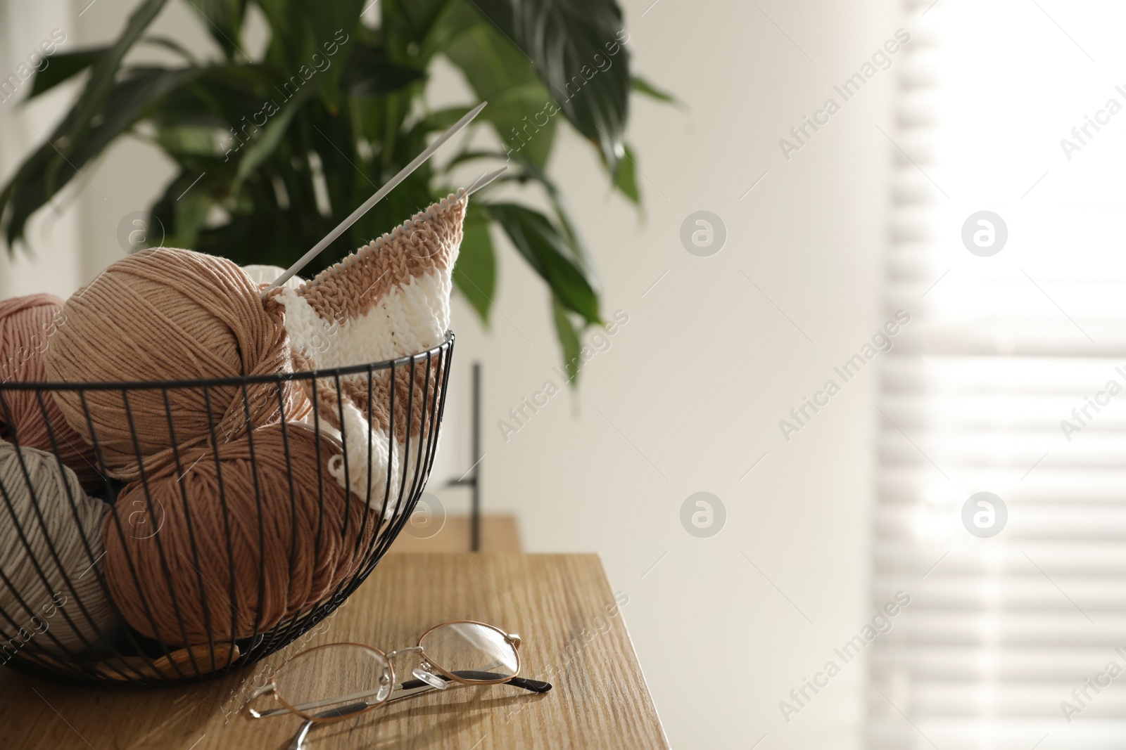 Photo of Glasses, yarn balls and knitting needles on wooden table indoors, space for text. Creative hobby