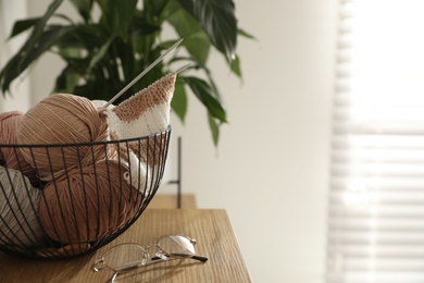 Glasses, yarn balls and knitting needles on wooden table indoors, space for text. Creative hobby