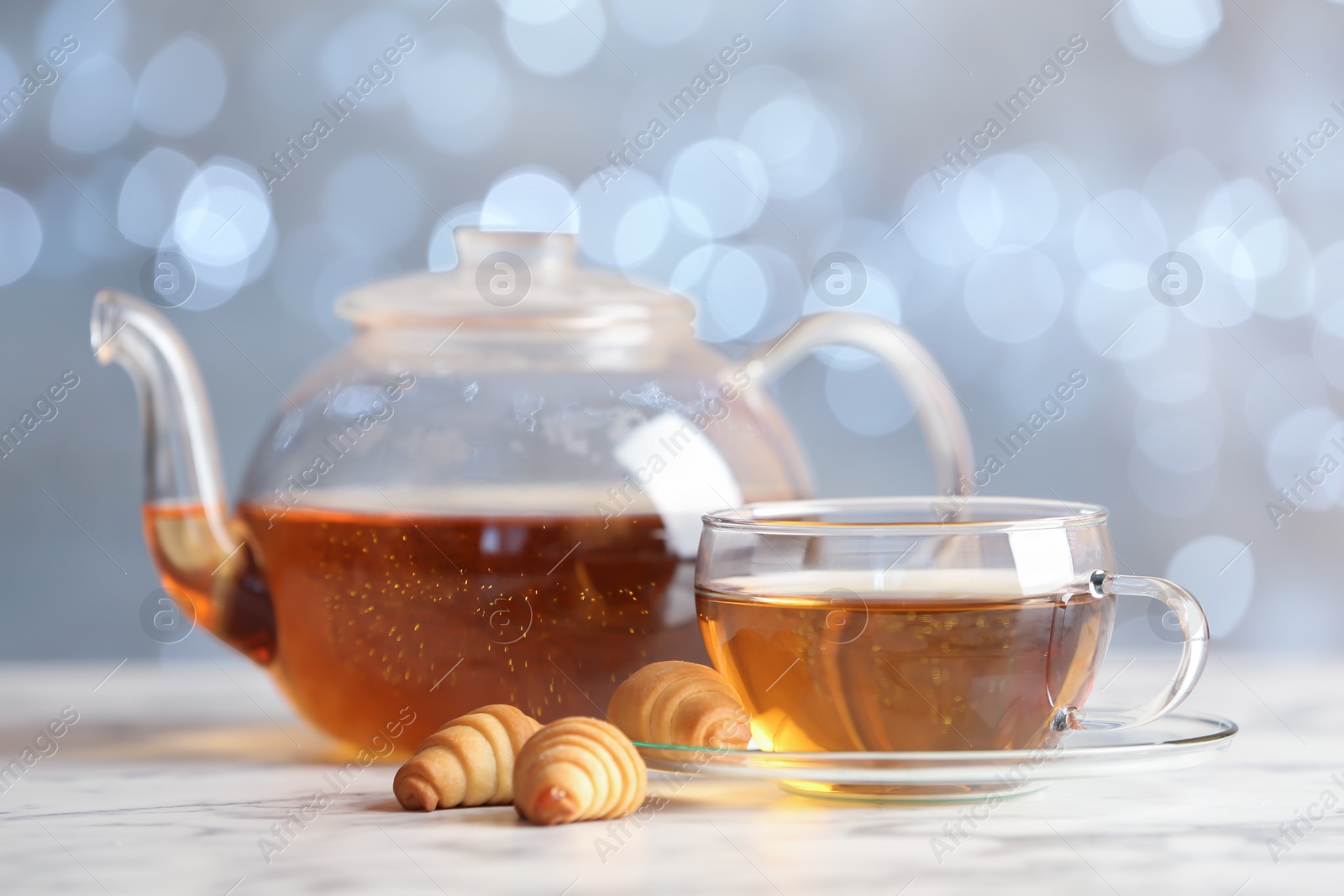 Photo of Glass cup and teapot with black tea on table against blurred lights