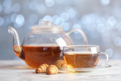 Photo of Glass cup and teapot with black tea on table against blurred lights