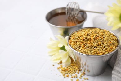 Fresh bee pollen granules and flowers on white table, closeup. Space for text