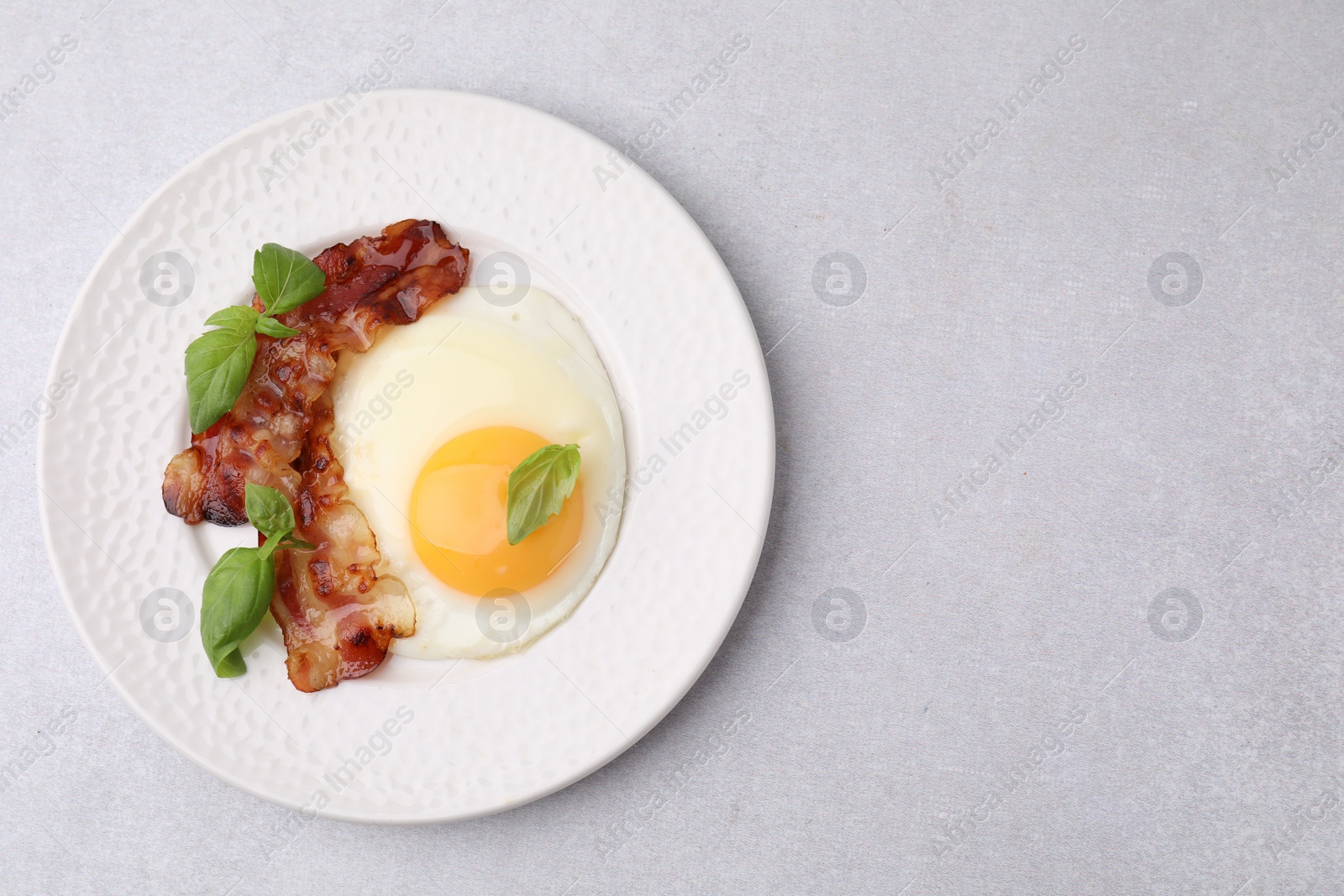 Photo of Fried egg, bacon and basil on light grey table, top view. Space for text