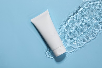 Tube of face cleansing product in water against light blue background, top view