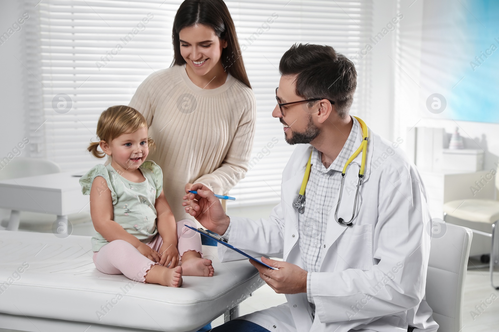 Photo of Mother and her cute baby having appointment with pediatrician in clinic. Doctor examining little girl