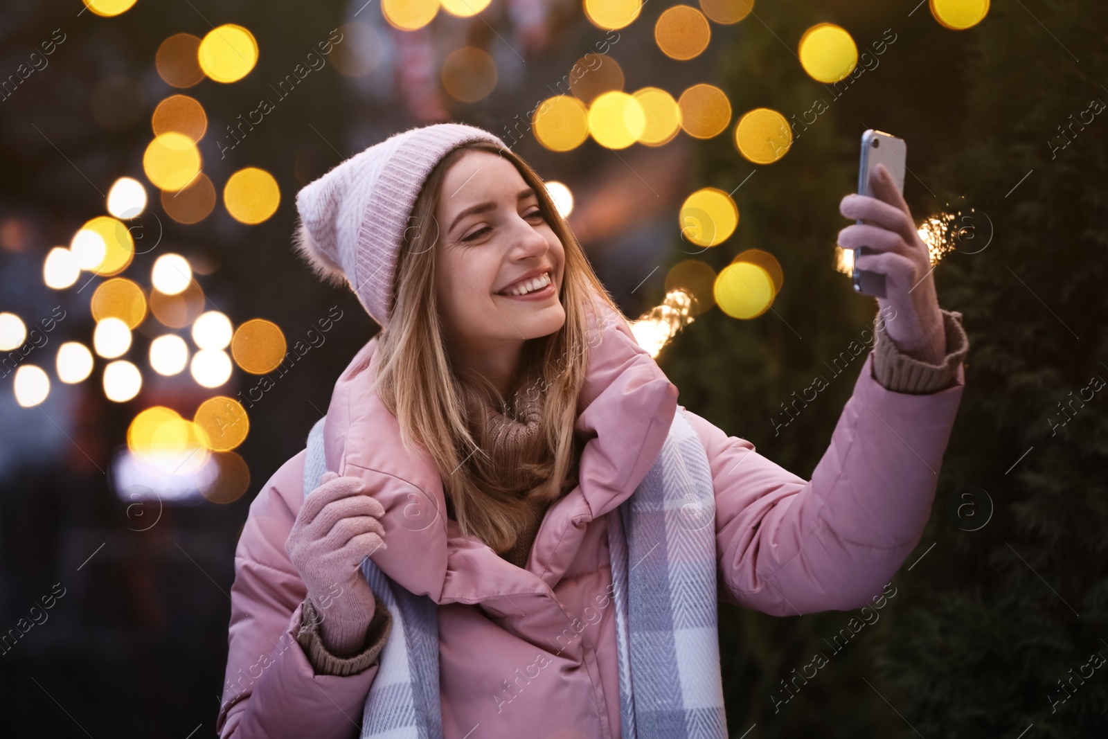 Photo of Happy young woman taking selfie outdoors in evening. Christmas celebration