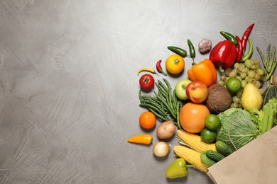 Paper bag with assortment of fresh organic fruits and vegetables on grey table, flat lay. Space for text