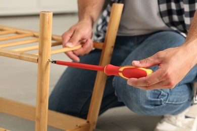 Photo of Man with screwdriver assembling furniture indoors, closeup