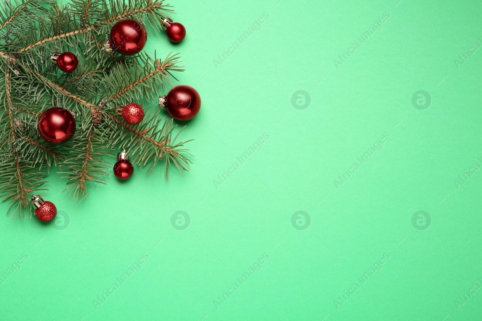 Photo of Fir branch with shiny Christmas balls on green background, top view. Space for text