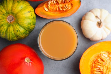 Photo of Tasty pumpkin juice in glass and different pumpkins on light grey table, flat lay