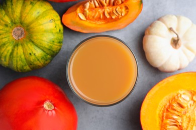 Tasty pumpkin juice in glass and different pumpkins on light grey table, flat lay