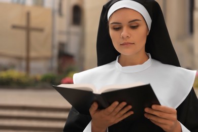 Photo of Young nun reading Bible outdoors, space for text