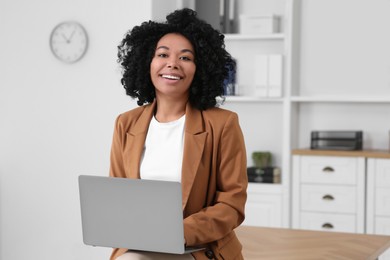 Smiling young businesswoman using laptop in modern office