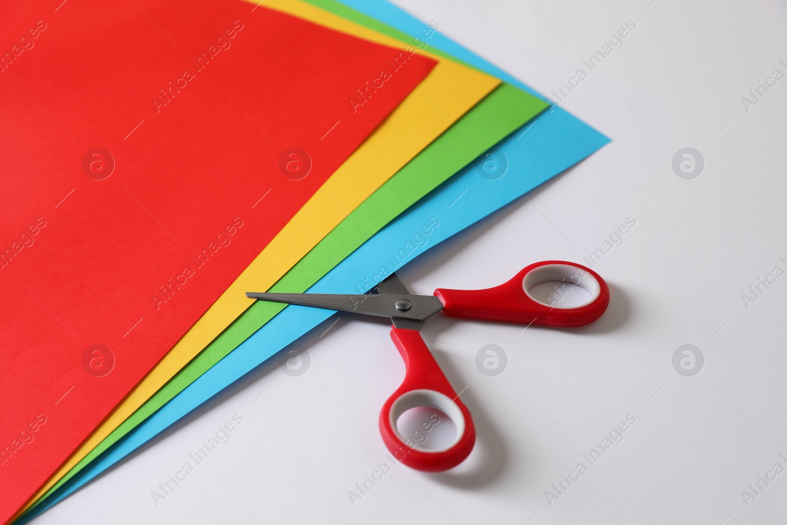 Photo of Red scissors and color sheets of paper on white background