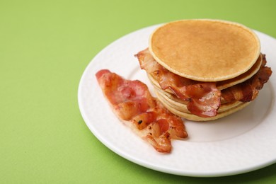 Delicious pancakes with bacon on green table, closeup. Space for text