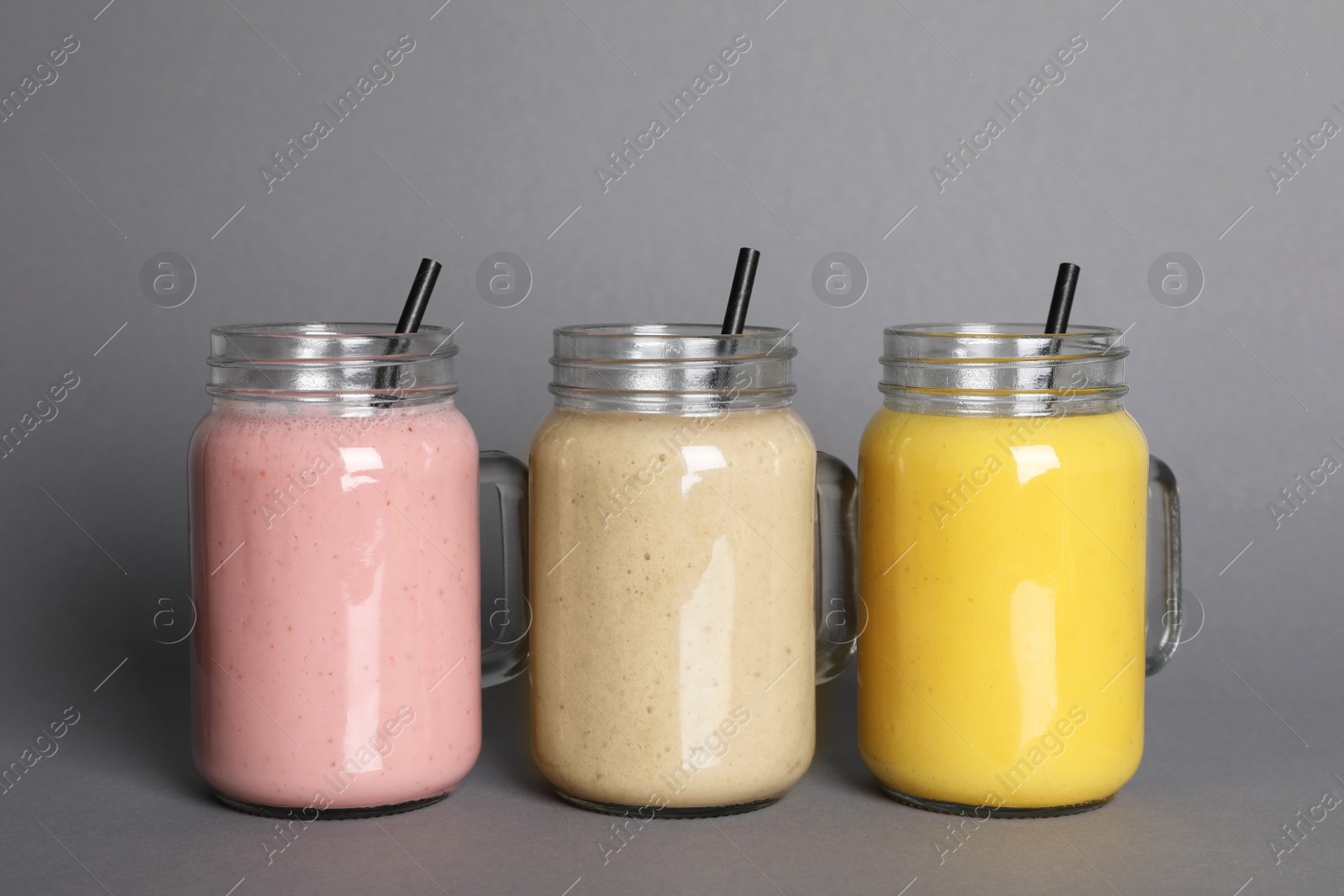 Photo of Mason jars with different smoothies on grey background