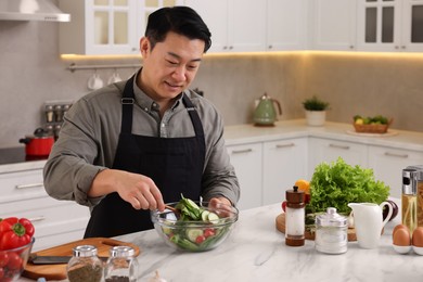 Photo of Man cooking fresh salad at countertop in kitchen