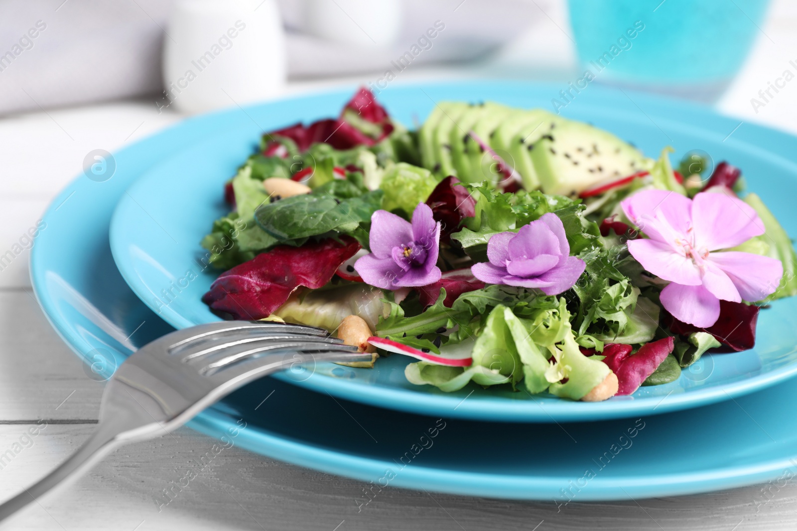 Photo of Fresh spring salad with flowers served on white wooden table, closeup