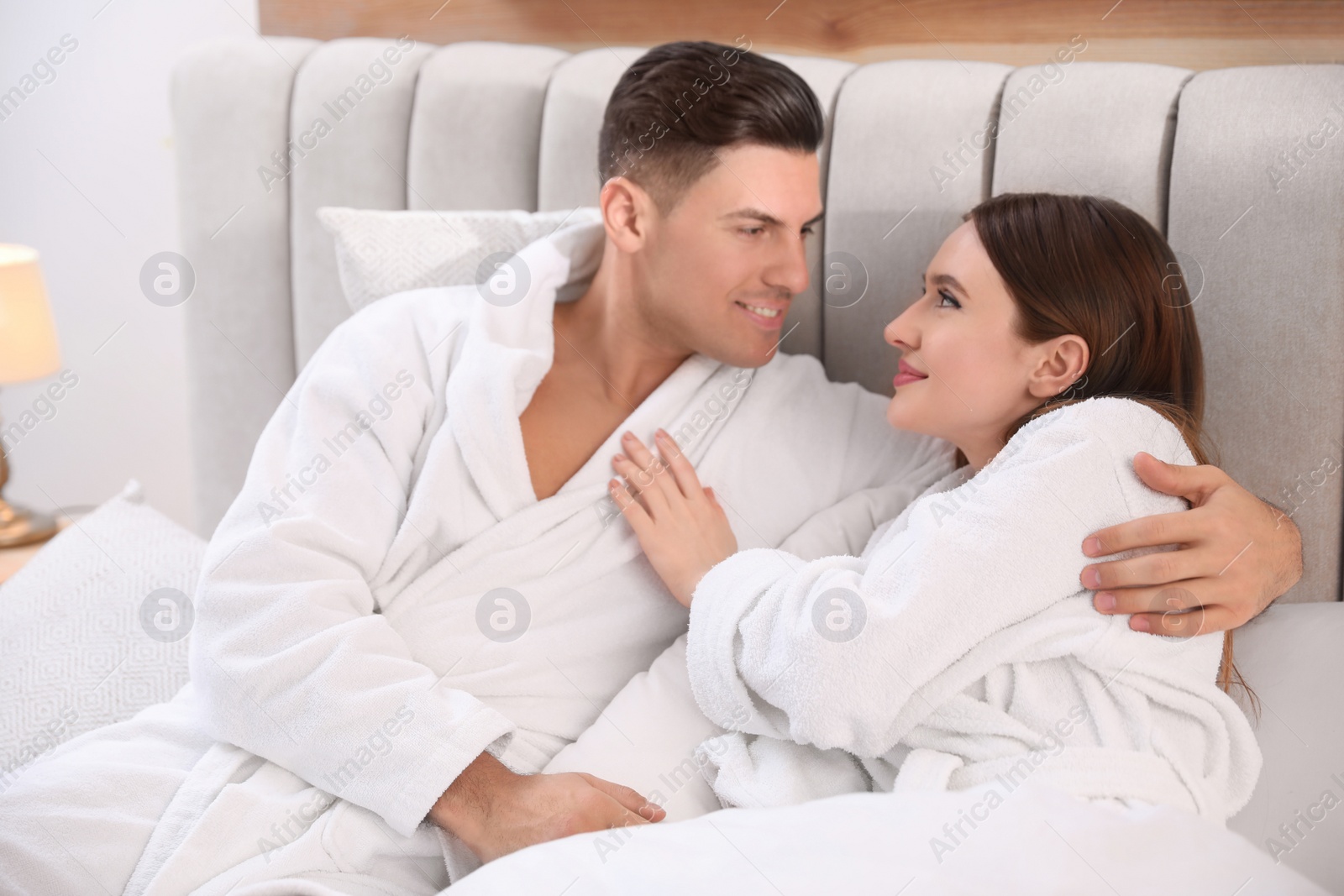 Photo of Happy couple in bathrobes resting on bed at home