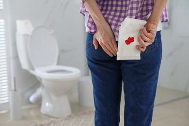 Woman holding toilet paper with blood stain in rest room, closeup. Hemorrhoid concept