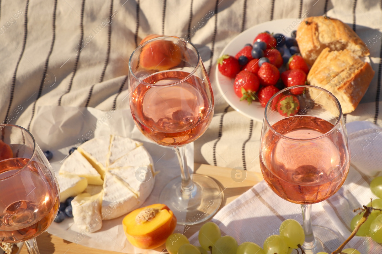 Photo of Glasses of delicious rose wine and food on white picnic blanket