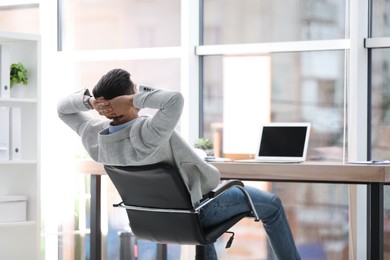 Photo of Businessman relaxing in office chair at workplace, back view. Space for text