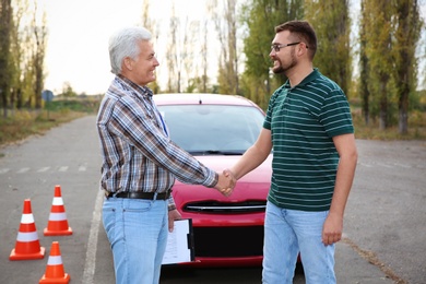 Happy man shaking hands with senior instructor outdoors. Get driving license