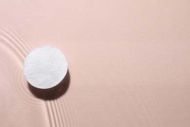 Cotton pad in micellar water on beige background, top view. Space for text