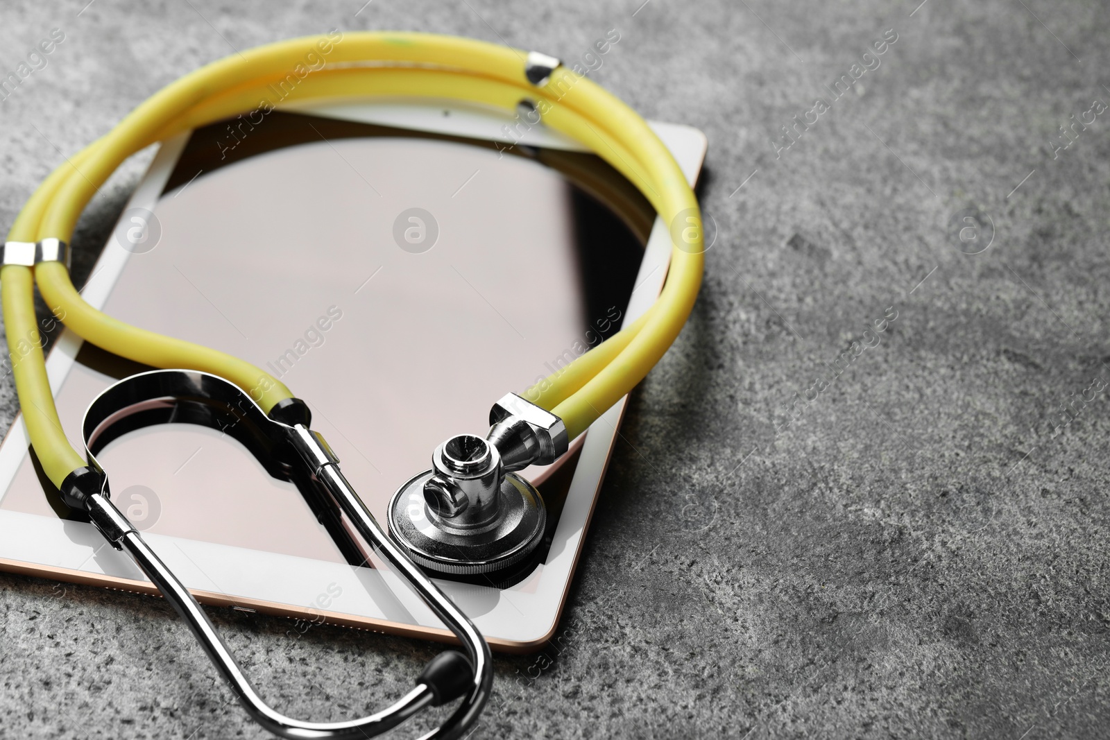 Photo of Modern tablet and stethoscope on grey table, closeup. Space for text