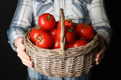 Woman with basket of ripe tomatoes on black background, closeup