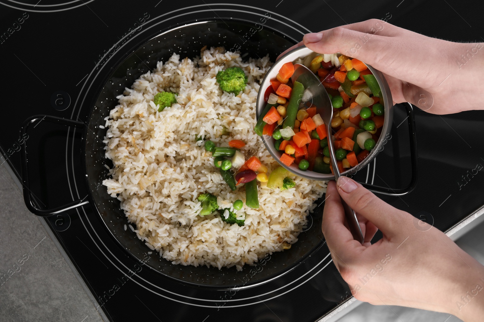 Photo of Woman cooking tasty rice with vegetables on induction stove, top view