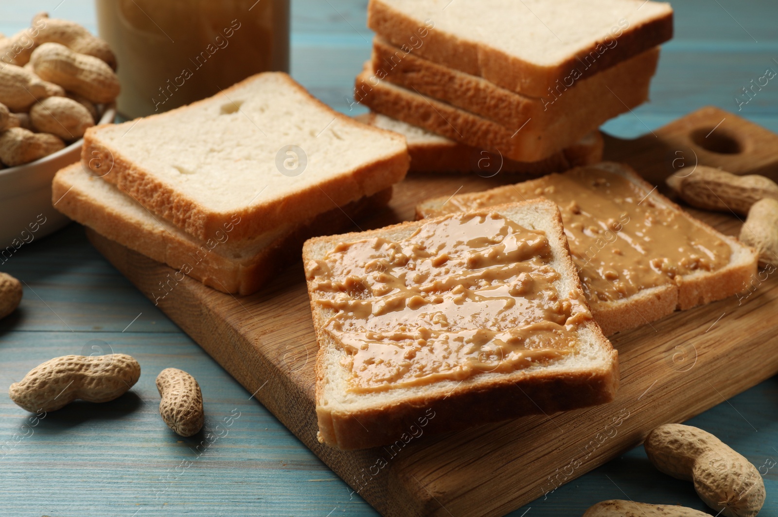 Photo of Delicious toasts with peanut butter and nuts on light blue wooden table