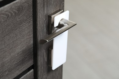 Photo of Wooden door with blank hanger on metal handle, closeup