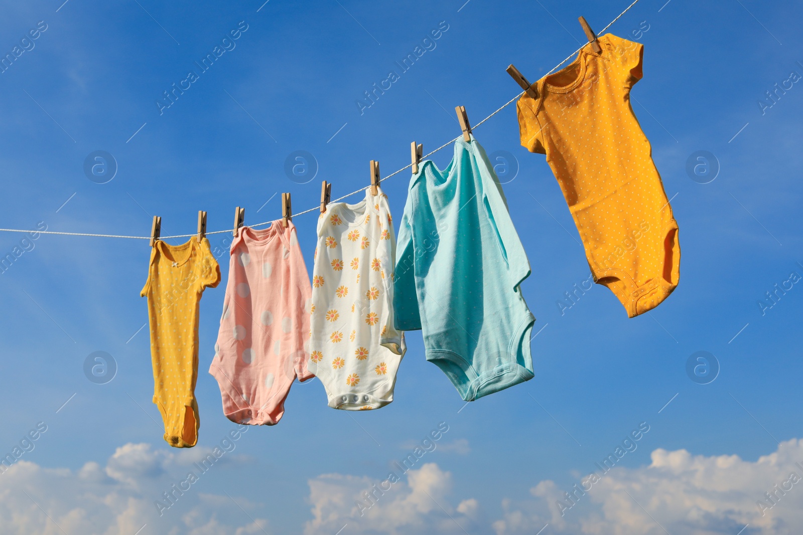 Photo of Clean baby onesies hanging on washing line against sky. Drying clothes