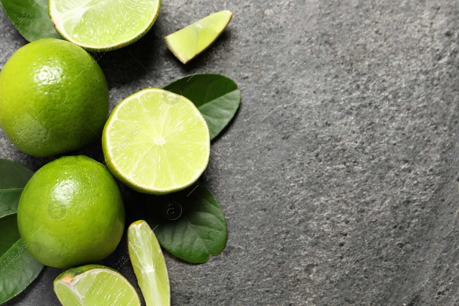 Photo of Fresh ripe limes and leaves on grey table, top view. Space for text