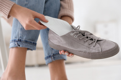 Photo of Woman putting orthopedic insole into shoe at home, closeup