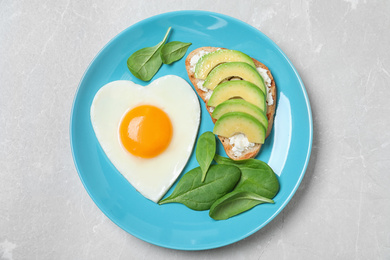 Photo of Romantic breakfast with heart shaped fried egg on light grey table, top view