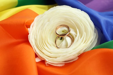 Wedding rings and flower on rainbow LGBT flag, closeup