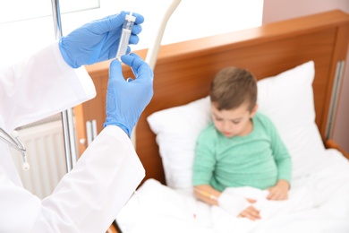 Photo of Doctor adjusting intravenous drip for little child in hospital, closeup