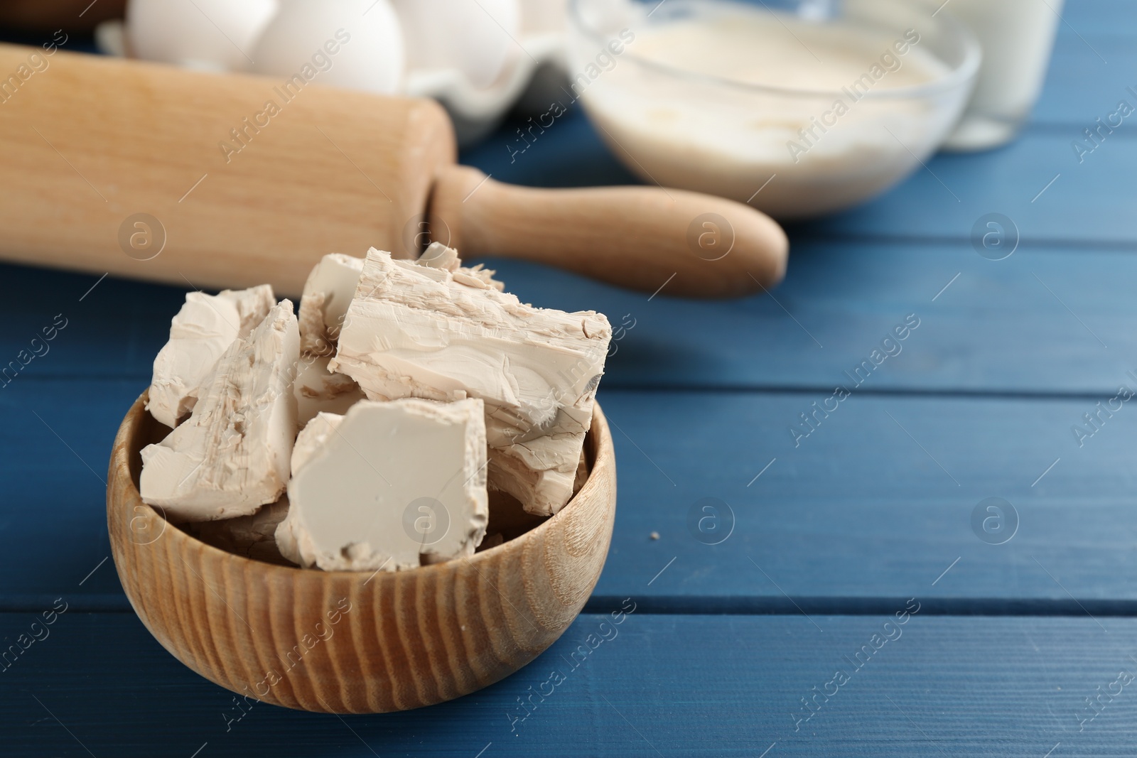 Photo of Pieces of compressed yeast in bowl on blue wooden table. Space for text