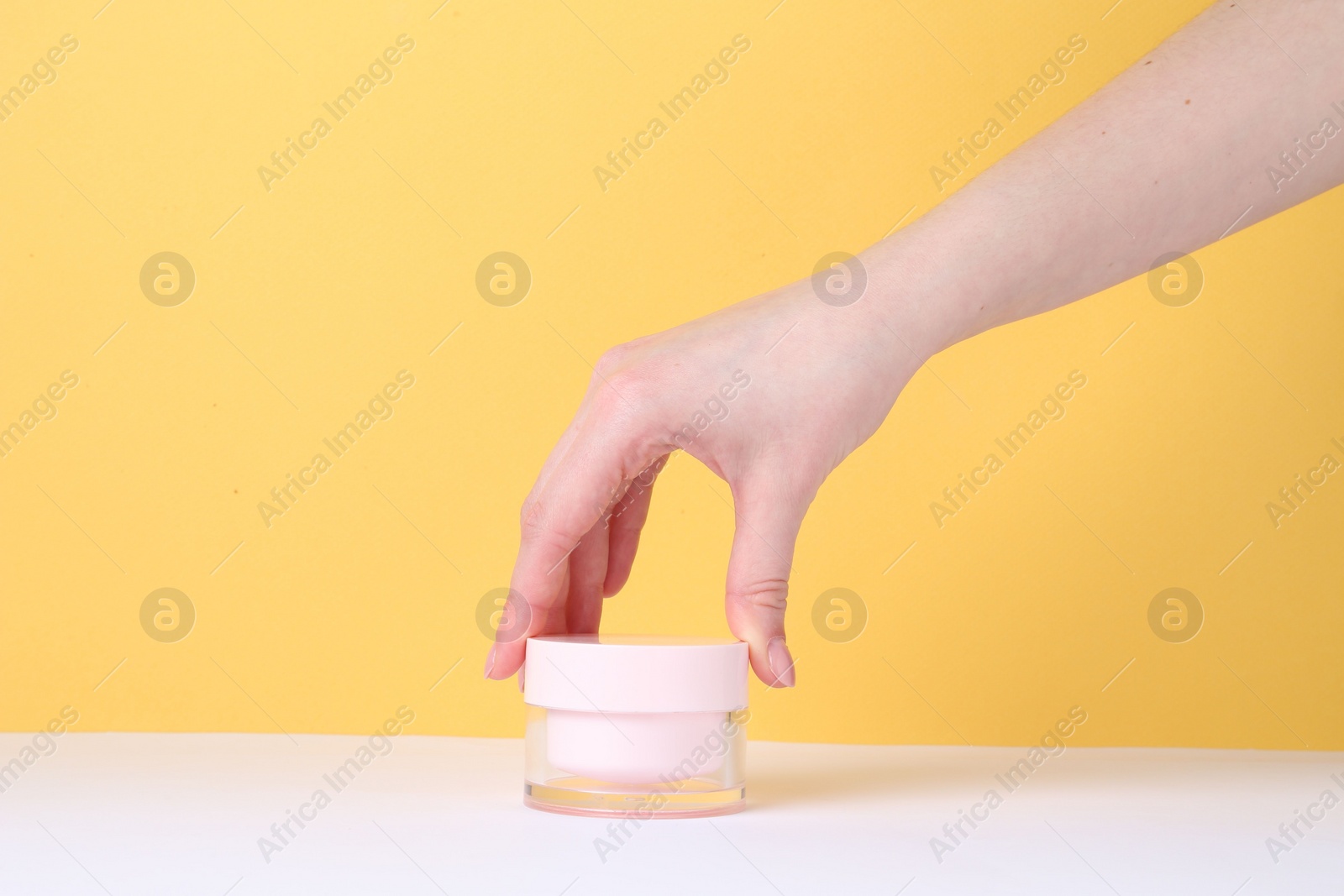 Photo of Woman with jar of cream on yellow background, closeup