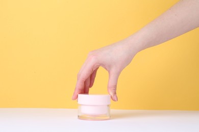 Woman with jar of cream on yellow background, closeup