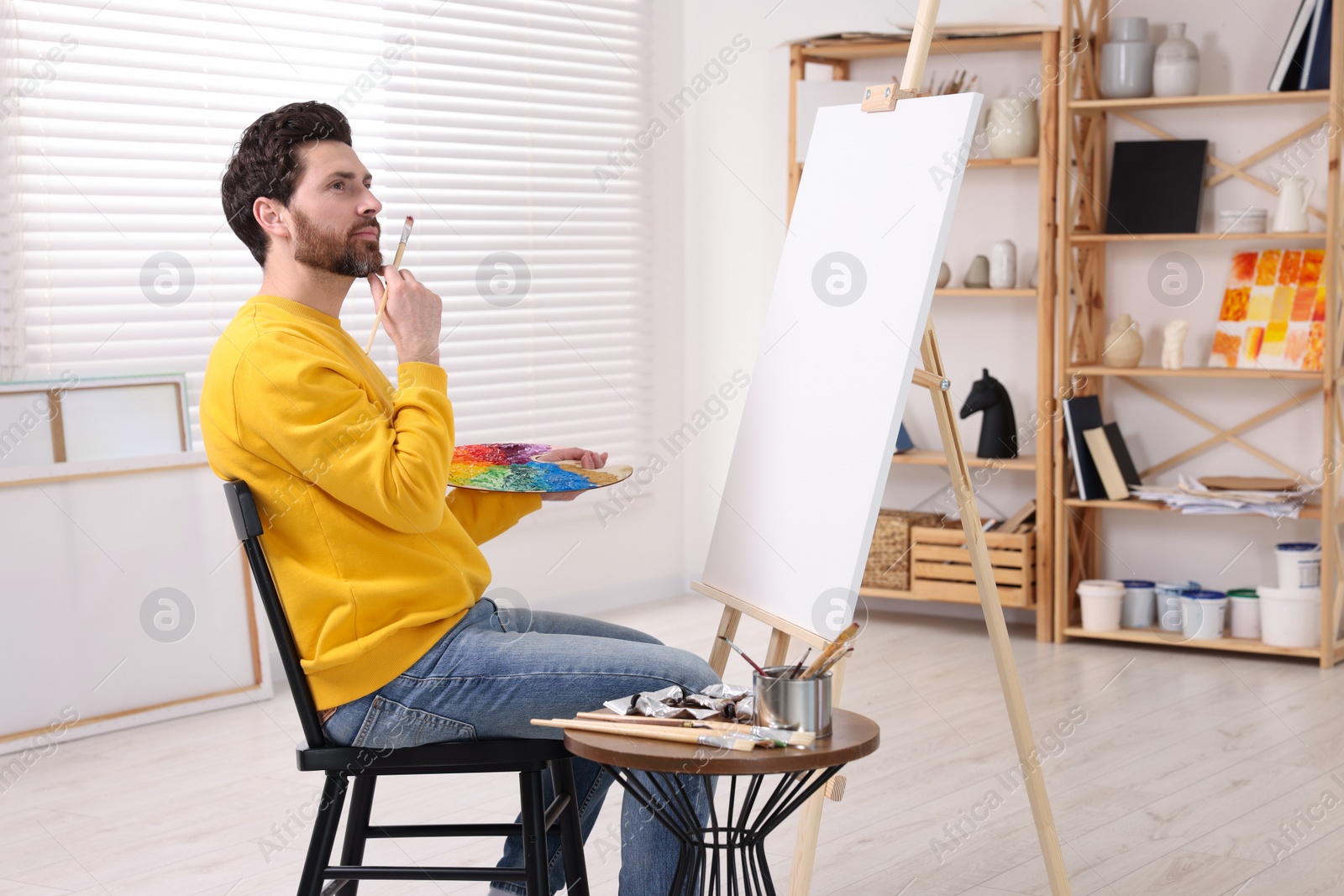 Photo of Man painting in studio. Using easel to hold canvas