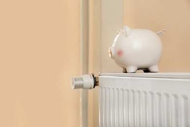 Photo of Piggy bank on modern heating radiator indoors
